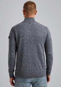 Grey knitted sweater with a high collar, ribbed cuffs, and hem. Features a small logo detail at the back and textured fabric. Casual fit.
