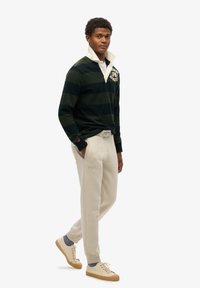 Groen en marineblauwe gestreepte pullover met een witte kraag, gecombineerd met beige sweatpants en lichte sneakers, met een gestructureerde stof.