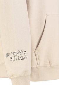 Beige sweatshirt gemaakt van zachte stof met een buidelzak, met zwart geborduurde tekst "GEEN GELD MAAR LIEFDE" op de mouw.
