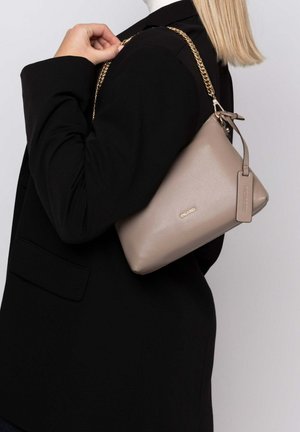 Beige Lederhandtasche mit strukturiertem Design, kombiniert mit einem goldenen Kettenriemen. Auffälliges Logo-Detail auf der Vorderseite und strukturierte Oberfläche.