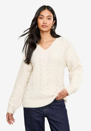 Cremefarbener V-Ausschnitt-Strickpullover mit Kabelmuster, langen Ärmeln und gerippten Bündchen. Weicher Stoff mit lockerer Passform und seitlichen Schlitzen am Saum.