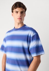 Camiseta de manga corta a rayas en diferentes tonos de azul y blanco, hecha de algodón suave, con un cuello redondo y un ajuste relajado.