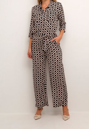 Combinaison noire et crème à motif losanges, manches longues, taille ceinturée et jambes larges. Caractéristiques : col et poches latérales.