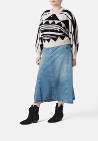 Minge cu model geometric alb și negru, asortată cu o fustă din denim în linie A și cizme negre din piele întoarsă cu vârf ascuțit.