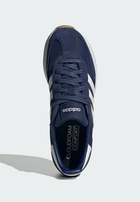 Marinblå sneakers med vita ränder och texturerat ovandel. Har standard snörning och vadderad sula märkt "CLOUDFOAM COMFORT". Rundad tå.