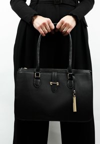 Zwarte leren handtas met gestructureerd ontwerp, dubbele handvaten, goudkleurige hardware en een kwastaccent. Voorzien van een ritssluiting en een vlakke bodem.