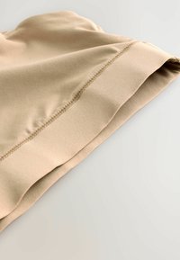 Close-up van beige stof met zichtbare naadsteken en omgevouwen zoom op een gladde, lichtgekleurde ondergrond.