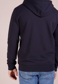 Marinblå hoodie i mjukt tyg, med en dragsko i huvan och ribbade ärmslut, som matchas med ljusblå jeans. Enkel och modern design.