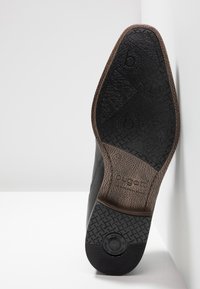 Férfi cipőtalp fekete gumiból, texturált felülettel, barna akcentussal a sarok közelében és egy logóval. Lapított kialakítás; tartós anyag.