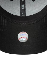 Gorra de béisbol negra con visera curva. Incluye una pegatina metálica redonda con un diseño de béisbol y la marca MLB en la visera.
