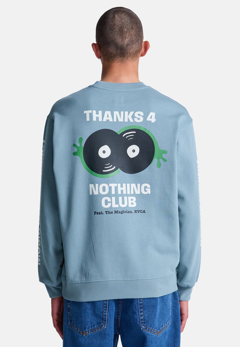 Osoba ubrana w jasnoniebieską bluzę z napisem "THANKS 4 NOTHING CLUB" oraz grafiką dwóch czarnych winylowych płyt z oczami na plecach.