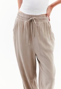 Pantalons beige fuselés avec une taille à cordon, présentant des rayures verticales, des poches et un tissu doux et texturé.