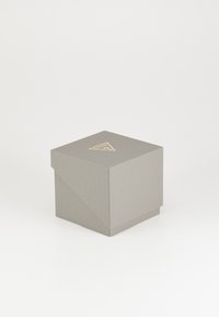 Grå papppresentförpackning med en strukturerad yta, där locket har ett triangulärt guldemblem och vinklade hörn.