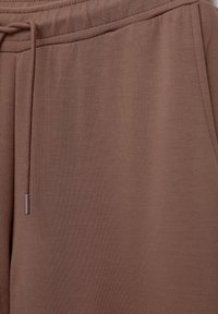 Brown jogging pants made of soft fabric, featuring an elastic waistband and drawstring with metal tips, displaying a smooth, matte texture.