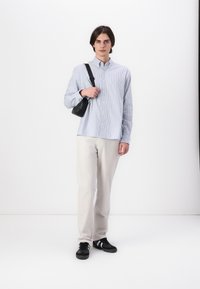 Camisa de botones a rayas azul claro y blanca; pantalones de color crema; zapatillas negras; bolso de hombro; textura de algodón suave; corte relajado.