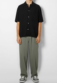 Czarna koszula z krótkim rękawem, kołnierzykiem zapinanym na guziki i kieszenią, w zestawie z luźnymi, oliwkowozielonymi spodniami oraz czarno-białymi trampkami.