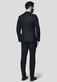 Czarny garnitur z dopasowaną marynarką o teksturowanej tkaninie i slim fit. Spodnie mają prosty krój, w zestawie z czarnymi butami.