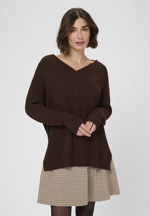 Brown ribbed sweater with a V-neck, wide sleeves, and a relaxed fit, paired with a beige checkered skirt. Textured knit detail throughout.