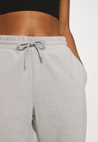 Hellgraue Fleece-Jogginghose mit elastischem Bund, dekorativem Kordelzug und seitlichen Taschen; weicher Stoff und lässige Passform.
