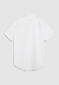 Chemise blanche à manches courtes avec col, vue de dos avec un yoke droit et un ourlet courbé sur un fond gris clair.