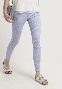 Leggings de color púrpura claro con pequeños patrones florales, que ofrecen un ajuste ceñido. Combinados con sandalias de metal plateado y un bolso cruzado gris.