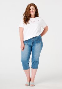 Chemise blanche à manches courtes avec des détails brodés, assortie à un pantalon capri en denim bleu clair, doté de poches arrière et d'ourlets retroussés.