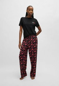 T-shirt nera con testo "HUG", abbinata a pantaloni neri larghi con un motivo a cuori rossi. Tessuto morbido, stile rilassato.