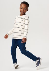 Witte langetermijnsleeve shirt met marineblauwe strepen, met een visborduring, gecombineerd met blauwe spijkerbroek. Sneakers maken de outfit compleet.