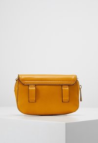 Borsa a mano gialla in pelle con forma strutturata, chiusura a patta magnetica, due cinturini anteriori e un compartimento con cerniera sul lato.