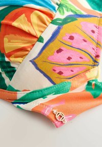 Farverigt stof med blomstermønster i klare orange, pink og grønne nuancer. Detaljeret med en grøn kant og en guldfarvet hardware-accent.