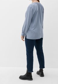 Helles blaues Langarmbluse mit gerafftem Rücken, seitlichen Schlitzen, getragen mit dunkelblauen Skinny-Jeans und schwarzen Ankle Boots. Glatte Stofftextur.