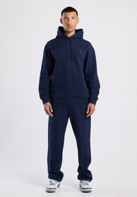Sudadera azul marino y pantalones de chándal a juego, hechos de una tela suave. Cuenta con un bolsillo frontal, capucha ajustable y puños elásticos en los pantalones.