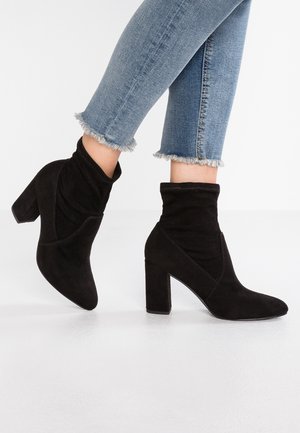Zwarte suède enkellaarsjes met een slouchy design, met een hak en puntige neus. Gecombineerd met cropped jeans met rafelige zoom.