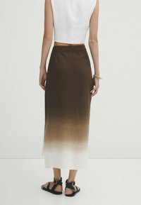 Jupe longue en lin avec un dégradé ombré du marron au blanc, taille ajustée et fente latérale. Portée avec des sandales noires.