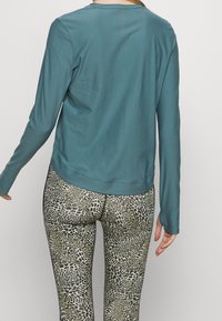 Türkises Langarmoberteil mit glatter Textur, kombiniert mit Leggings im Leopardenmuster, die einen dehnbaren Sitz und abwechslungsreiche Schwarz- und Grüntöne aufweisen.
