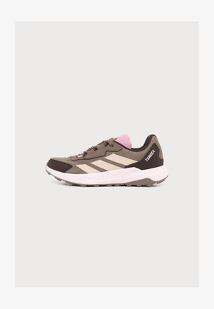Bruine en roze Adidas Terrex trailrunningschoen met beige strepen en een witte zool, zijaanzicht op een effen achtergrond.