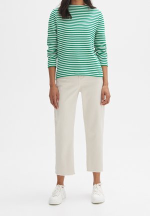 Grün-weiß gestreifter Strickoberteil mit drei Viertelärmeln, kombiniert mit hellbeigen Caprihosen und weißen Sneakern. Einfaches Design, lässige Passform.