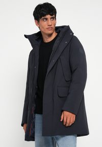 Mørkeblå parka med aftagelig hætte, frontlommer og lynlås. Glat tekstur, letvægtsdesign og kontrastfarvet inderside.
