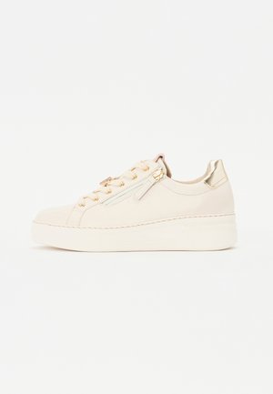 Zapatilla de cuero beige con superficie texturizada, hardware dorado y suela de plataforma. Presenta un zipper lateral y cordones decorativos.