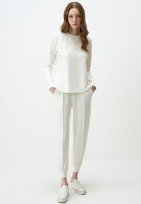 Witte lange mouwen top met geborduurde details en bijpassende joggerbroeken met elastische manchetten, aangevuld met witte sneakers.