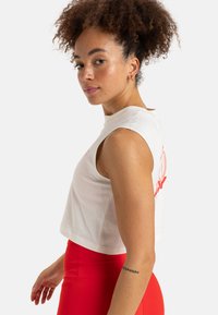 White cropped sleeveless top with a round neckline. Features red graphic design on the front. Worn with high-waisted red leggings.