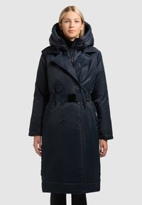 Temno modri dolg plašč z dvojnimi zapenjanji, velikim kapuco, pasom v predelu pasu in gladko, sijočo teksturo. Ima zadrgo in gumbno zapiranje.