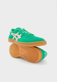 Roheline sametjalanõude jalats roosade aktsentidega, suletud paeltega ja kummist tallaga, millel on ringjate mustritega mustrid. ASICS logo kontsapatsil.