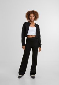 Fekete, gombos, rövidített kardigán magas derekú fekete nadrággal párosítva. Alatta fehér, testhez simuló atléta. Puha anyag, kényelmes, lazább szabás.