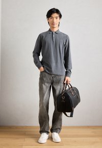 Γκρι μακρυμάνικο πόλο μπλούζα με γιακά, σε συνδυασμό με ξεθωριασμένο γκρι τζιν και λευκά αθλητικά παπούτσια. Κουβαλάει μια μαύρη δερμάτινη τσάντα duffel με καφέ λεπτομέρειες.