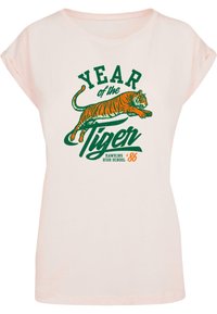 Lichtroze t-shirt met korte oprol mouwen, met een grote groene en oranje grafiek van een tijger en de tekst: "JAAR van de Tijger" en "HAWKINS HIGH SCHOOL '86."