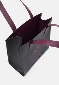 Zwarte synthetische tote bag met bordeauxrode banden; heeft een open bovenkant en een gestructureerde buitenkant; binnenkant gevoerd in bordeauxrood, geen extra hardware.