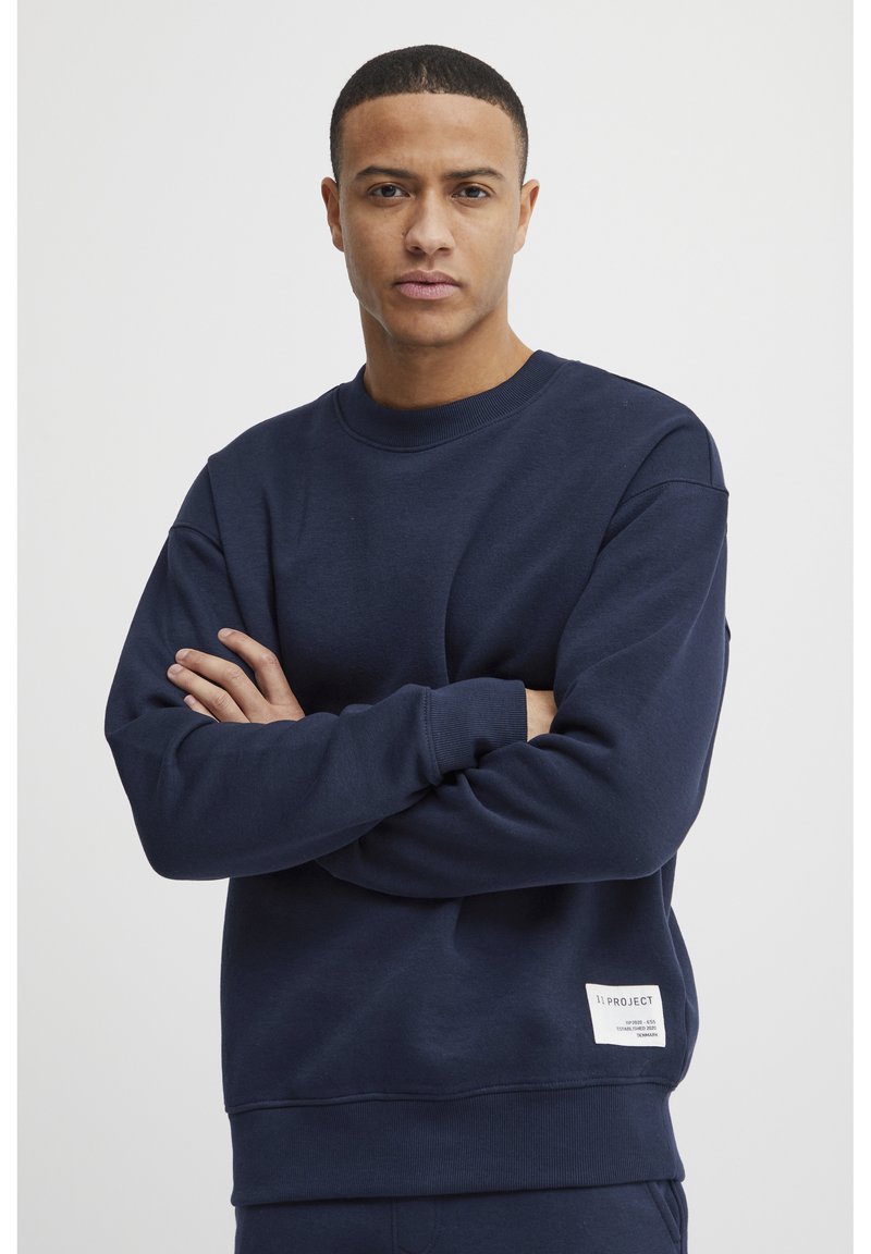 Marineblå sweatshirt laget av et mykt stoff, med rund hals, ribbede mansjetter og en merkelappdetalj på den nederste kanten. Avslappet passform.