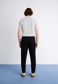 Grijze t-shirt met korte mouwen en zwarte broeken. De broeken hebben een elastische tailleband. Draagt witte en bruine sneakers met een gele accent.