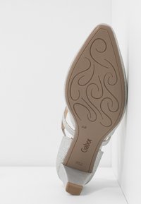Chaussure à paillettes argentées à bout ouvert avec un petit talon bloc, dotée d'une tige texturée et d'une semelle à motif détaillé. Marque visible sur la semelle.